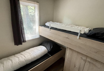 Habitación con literas y ventana con cortina oscura en Tiny Lodge Basic del Bungalowpark Het Verscholen Dorp, Países Bajos.