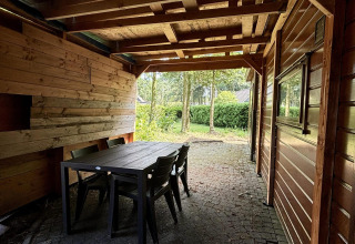 Zona exterior cubierta con paredes de madera, mesa y sillas en Tiny Lodge Basic, Het Verscholen Dorp.