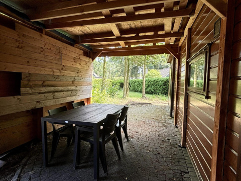 Zona exterior cubierta con paredes de madera, mesa y sillas en Tiny Lodge Basic, Het Verscholen Dorp.