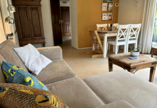 Salón acogedor en Tiny Lodge Basic con sofá, cojines coloridos, mesa de madera y comedor en Het Verscholen Dorp.