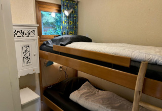 Kleine kamer met stapelbed, houten trap, raam met gordijn en witte kast in de Tiny Lodge Basic lodge.