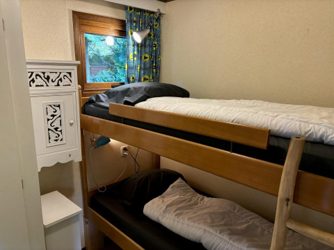 Pequeña habitación con litera, escalera de madera, ventana con cortina y armario en Tiny Lodge Basic.