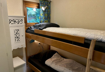 Piccola stanza con letto a castello, scala in legno, finestra con tenda e mobile bianco al Tiny Lodge Basic.