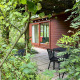 Hyggelig Tiny Lodge Basic med træbeklædning, stor glasdør og terrasse i grøn frodig have.