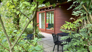 Knusse Tiny Lodge Basic met houten gevel, grote glazen deur en terras omringd door groene tuin.