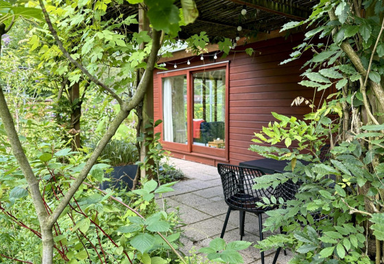 Acogedora Tiny Lodge Basic de madera, gran puerta de cristal y terraza rodeada de vegetación frondosa.