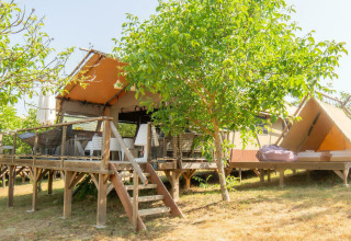 Safari-Zelt Desert Lodge mit privatem Bad, Holzterrasse, sonniger Wiese und Bäumen im Freien.