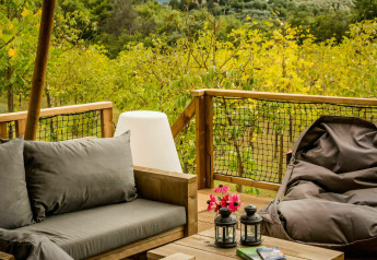 Buitenlounge op het terras van een safaritent met zetel, zitzak en lantaarns, omgeven door natuur.