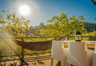 Terrazza soleggiata della tenda safari Desert Lodge al Camping Pian di Boccio, Italia, con amaca e tavolo.