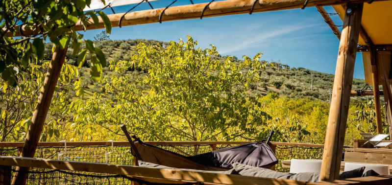 View from safari tent with hammock, wooden frame, and lush hills at Camping Pian di Boccio, Italy.