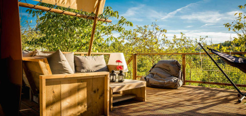 Terraza de la tienda Desert Lodge con sofá, puff y vistas a árboles verdes en Camping Pian di Boccio, Italia.