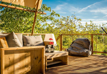 Terraza de la tienda Desert Lodge con sofá, puff y vistas a árboles verdes en Camping Pian di Boccio, Italia.