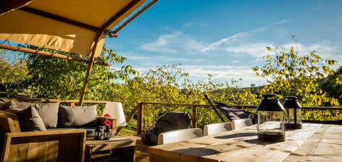 Zona de estar exterior junto a la tienda Desert Lodge con muebles de madera y vistas verdes en Camping Pian di Boccio.