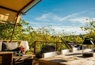 Zona de estar exterior junto a la tienda Desert Lodge con muebles de madera y vistas verdes en Camping Pian di Boccio.