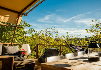 Zona de estar exterior junto a la tienda Desert Lodge con muebles de madera y vistas verdes en Camping Pian di Boccio.