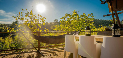 Terraza soleada con hamaca y sillas en la tienda Desert Lodge en Camping Pian di Boccio, Italia.