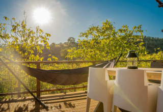 Zonnig terras met hangmat en stoelen bij Desert Lodge safaritent, Camping Pian di Boccio, Italië.
