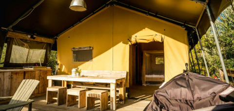 Safari Lodge tent op Camping Pian di Boccio in Italië met houten meubilair en zonnige ingang.