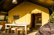 Safari Lodge tent op Camping Pian di Boccio in Italië met houten meubilair en zonnige ingang.