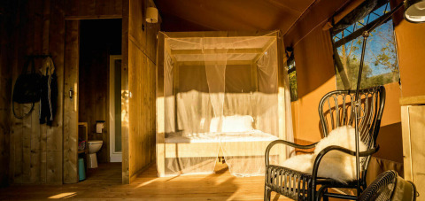 Interior of the Desert Lodge safari tent with a private bathroom, canopy bed and cozy chair in Italy.