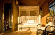 Interior of the Desert Lodge safari tent with a private bathroom, canopy bed and cozy chair in Italy.