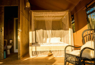 Interior of the Desert Lodge safari tent with a private bathroom, canopy bed and cozy chair in Italy.