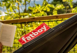 Persoon leest een boek in een zwarte Fatboy-hangmat bij Safari Lodge, Camping Pian di Boccio in Italië.