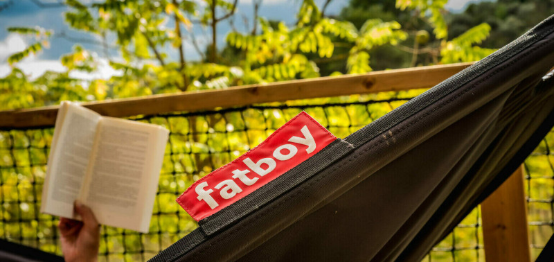 Person liest ein Buch in einer schwarzen Fatboy-Hängematte bei Safari Lodge, Camping Pian di Boccio, Italien.