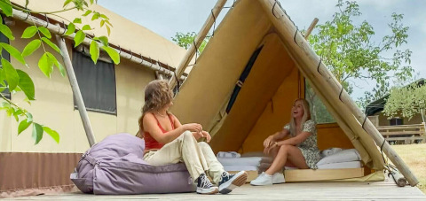 Dos mujeres disfrutan frente a una tienda tipo safari Desert Lodge en Camping Pian di Boccio, Italia.