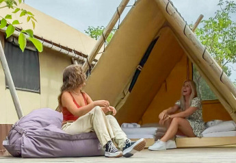 Two women relax outside a Desert Lodge safari tent with private bathroom at Camping Pian di Boccio, Italy.