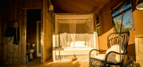 Interior de tienda safari con cama con dosel y baño privado en Camping Pian di Boccio en Italia.