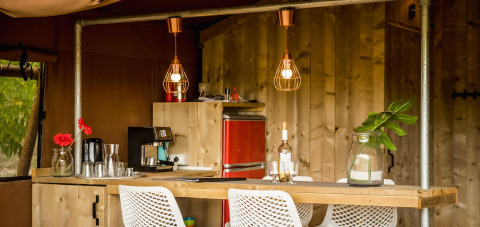 Modern safari tent kitchen with wooden furniture and red fridge at Camping Pian di Boccio, Italy.
