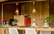 Modern safari tent kitchen with wooden furniture and red fridge at Camping Pian di Boccio, Italy.