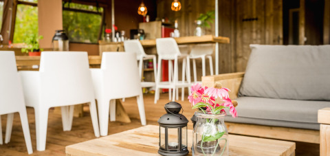 Cozy indoor area of a safari tent with wooden furniture, flowers in a glass jar, and modern decor.