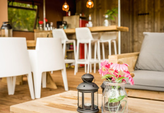 Area interna accogliente di una tenda safari con arredi in legno, fiori in vaso e decorazione moderna.