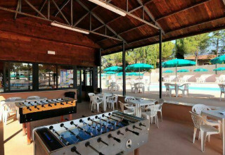 Espace couvert avec baby-foot et tables, vue sur piscine et parasols au Camping Pian di Boccio en Ombrie, Italie.