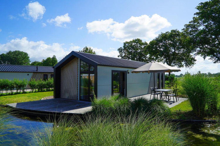 Refugio moderno junto al lago con terraza al aire libre, sombrilla y rodeado de vegetación.