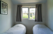 Lichte slaapkamer met twee enkele bedden en raam in Berkel-lodge bij EuroParcs Veluwemeer, Nederland.