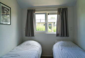 Lichte slaapkamer met twee enkele bedden en raam in Berkel-lodge bij EuroParcs Veluwemeer, Nederland.