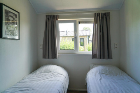 Dormitorio luminoso con dos camas individuales y ventana en la cabaña Berkel de EuroParcs Veluwemeer, Países Bajos.