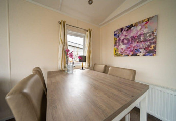 Eettafel met vier stoelen, bloemdecoratie en kunstwerk in de Berkel-lodge bij EuroParcs Veluwemeer.