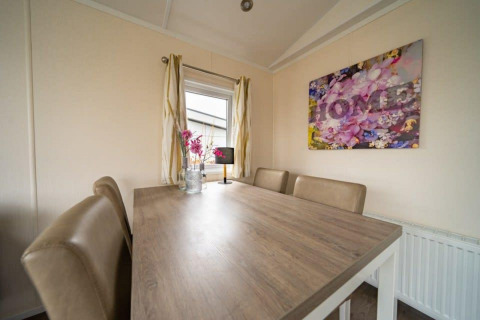 Mesa de comedor con cuatro sillas beige y arte floral en la pared en el lodge Berkel de EuroParcs Veluwemeer.