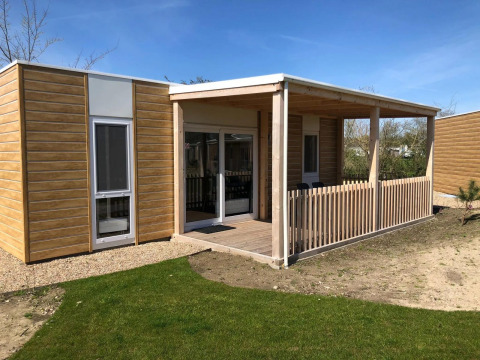 Eine moderne Lodge namens Cosy Unique mit Holzfassade, überdachter Terrasse und grünem Rasen davor.