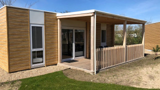 Een eigentijdse lodge met de naam Cosy Unique, houten bekleding, overdekt terras en een grasveld vooraan.