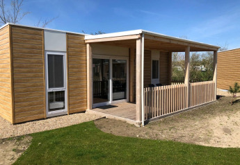 Een eigentijdse lodge met de naam Cosy Unique, houten bekleding, overdekt terras en een grasveld vooraan.
