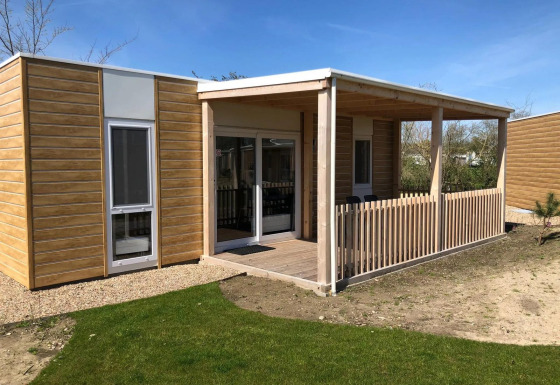 Een eigentijdse lodge met de naam Cosy Unique, houten bekleding, overdekt terras en een grasveld vooraan.