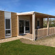 En moderne lodge ved navn Cosy Unique med træfacade, overdækket terrasse og grøn græsplæne foran.