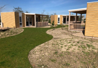 Buitenfoto van de Cosy Unique lodge bij EuroParcs Veluwemeer in Nederland met houten huisjes en graspaadjes.