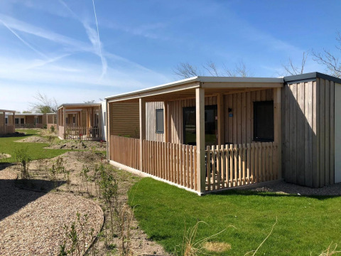 Außenaufnahme von Holzhütten der Cosy Unique Lodge mit Veranden, grünen Rasenflächen und blauem Himmel.