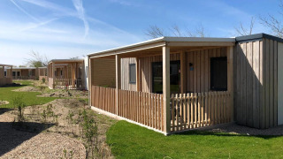 Buitenbeeld van houten lodges bij Cosy Unique met veranda’s, groene gazons en heldere blauwe lucht.